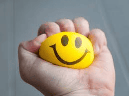 A collage of two images: on the left, a hand tightly squeezes a yellow smiley face stress ball, while on the right, alongside a mesh stress ball filled with silica gel, another hand squishes a second similar mesh stress ball.